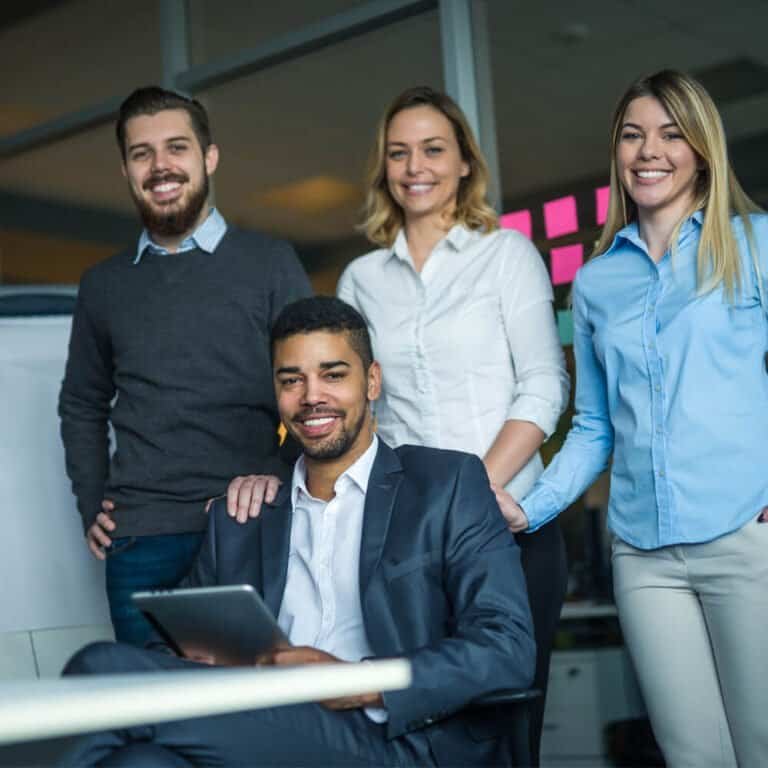 Team of four business professionals smiling in a modern office environment.